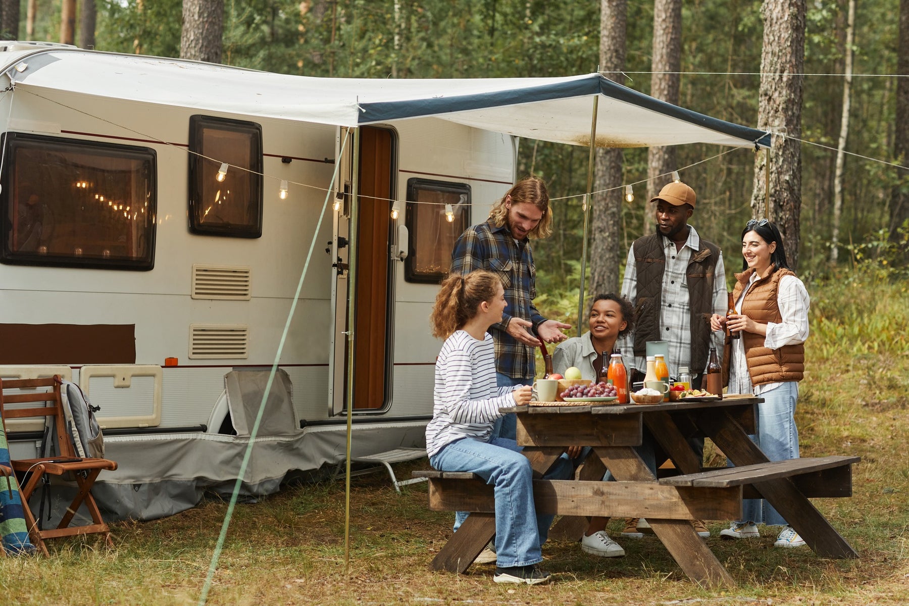 A group of friends sitting at a campsite picnic table outside of an RV