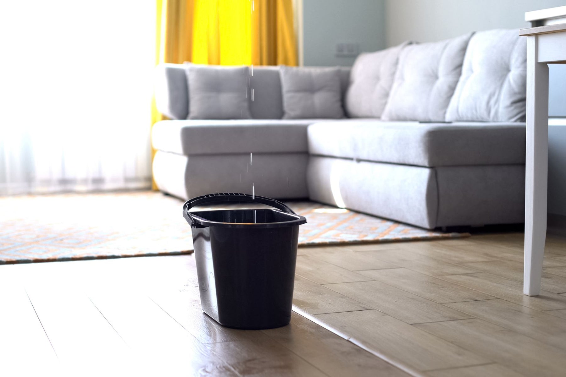 A black water bucket catching water from underneath a ceiling leak