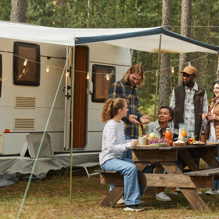 A group of friends sitting at a campsite picnic table outside of an RV